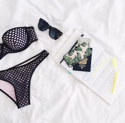 Fashionable flat lay of travel essentials on a sandy beach.
